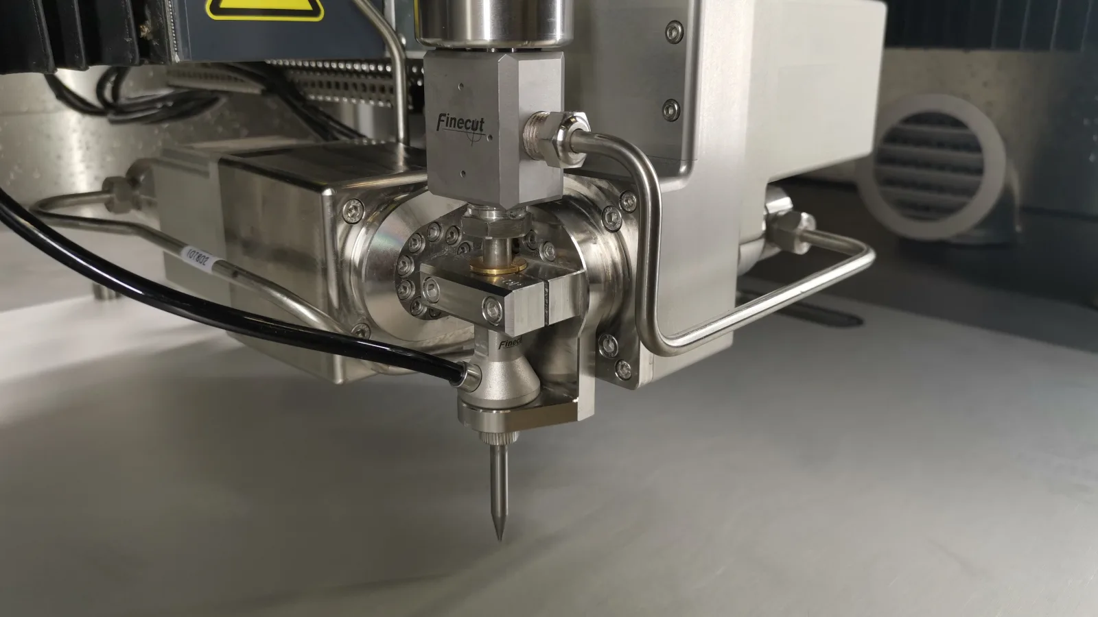 Close-up of the Finecut ABX five-axis cutting head, nozzle lowered over the work table