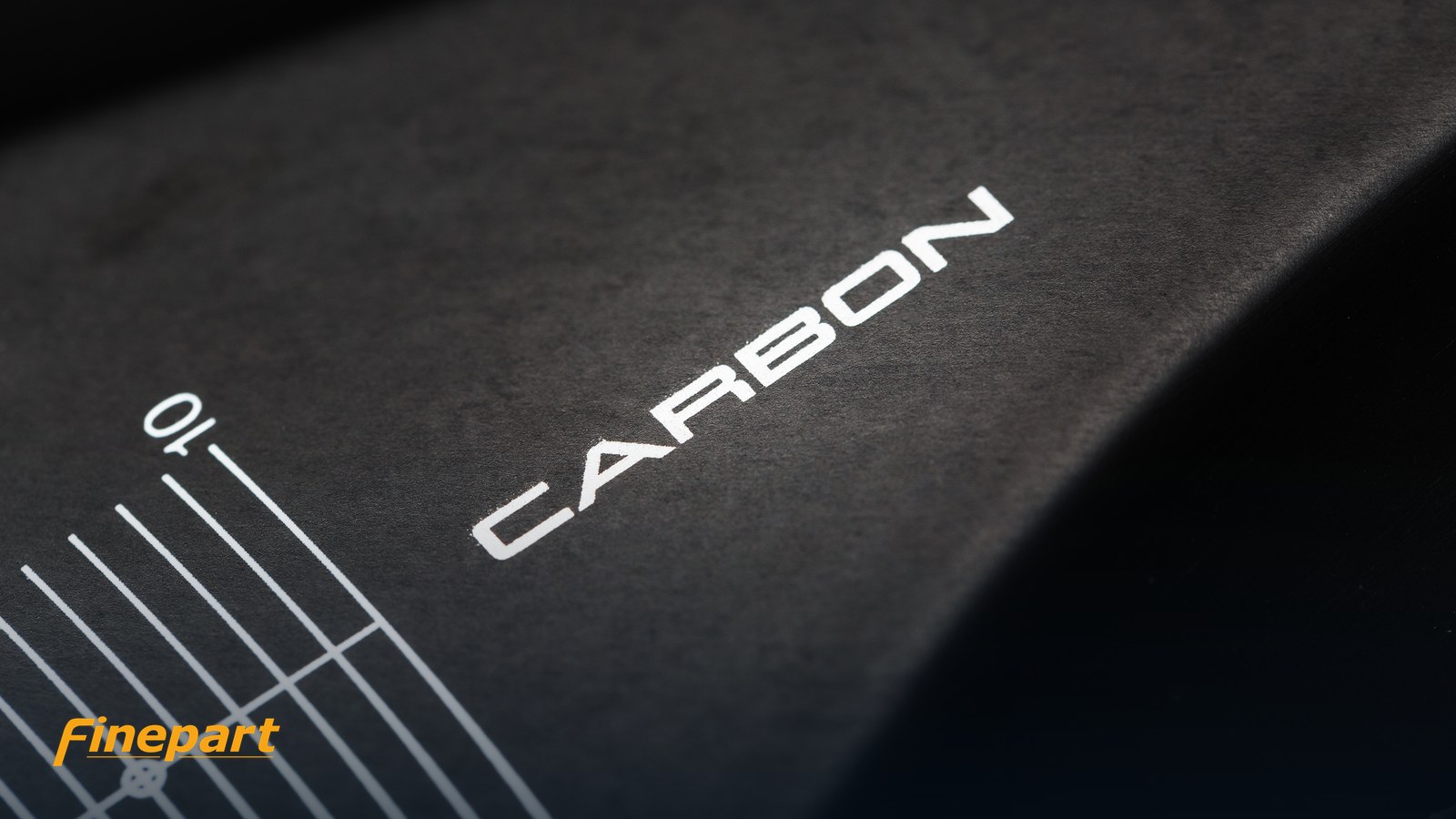 Carbon fibre composite surface beside a precision rule, illustrating the materials that crack or delaminate under mechanical tools